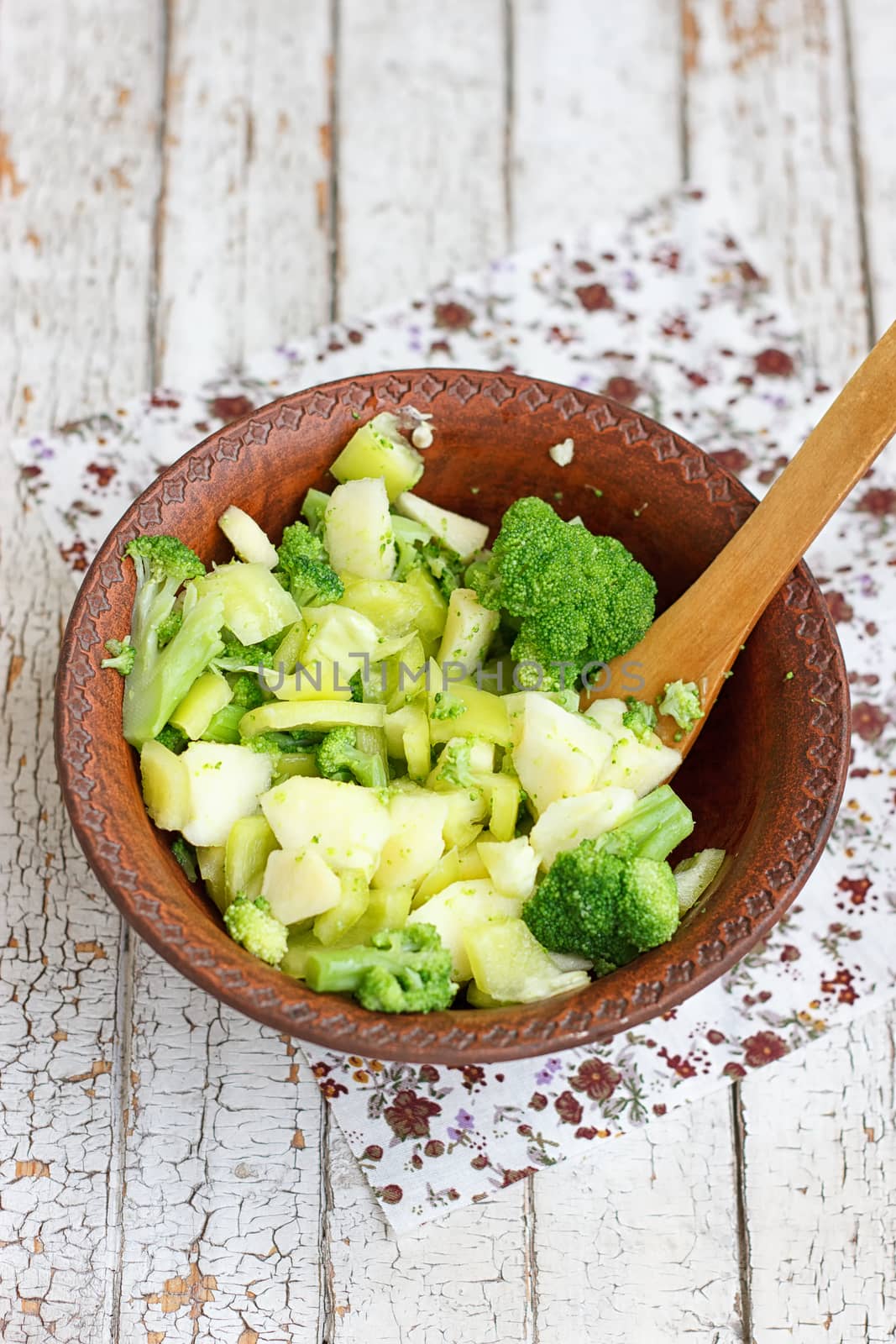Salad in a deep bowl, broccoli, pepper and apple. On a wooden background
