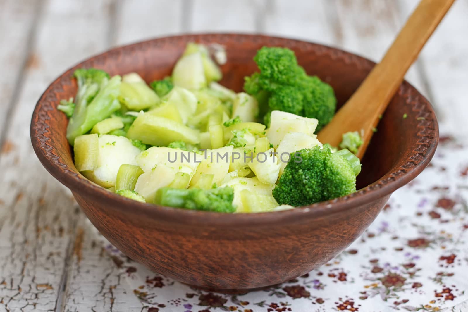 Salad in a deep bowl, broccoli, pepper and apple. On a wooden background