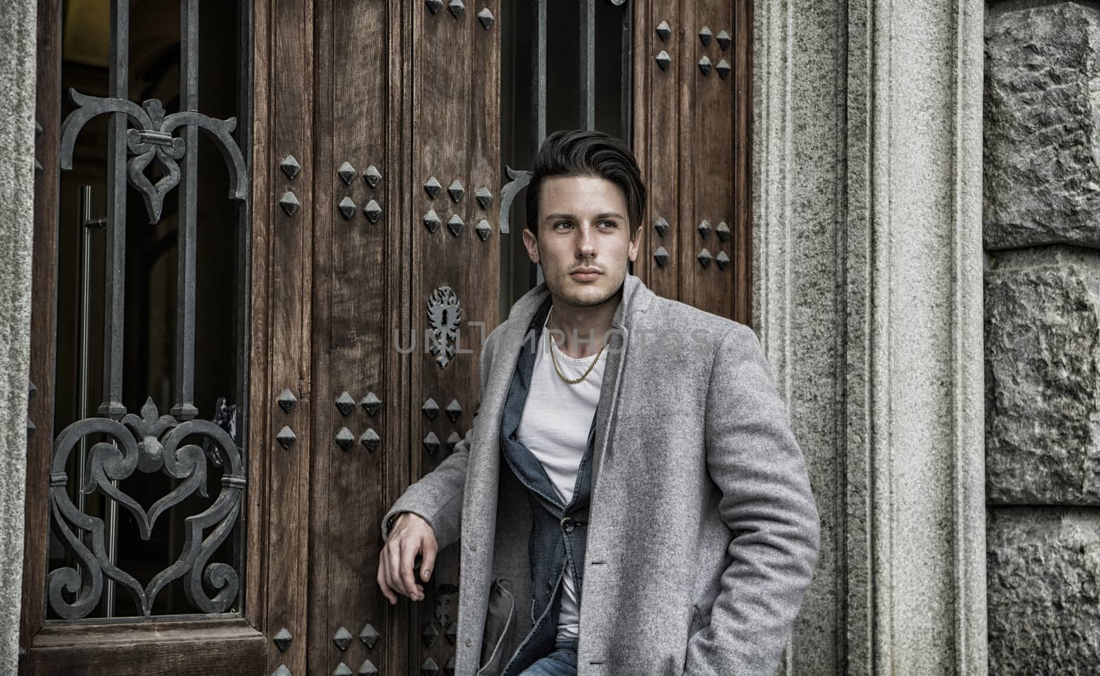 Elegant attractive young man outdoor wearing wool coat, in European city, looking away to a side