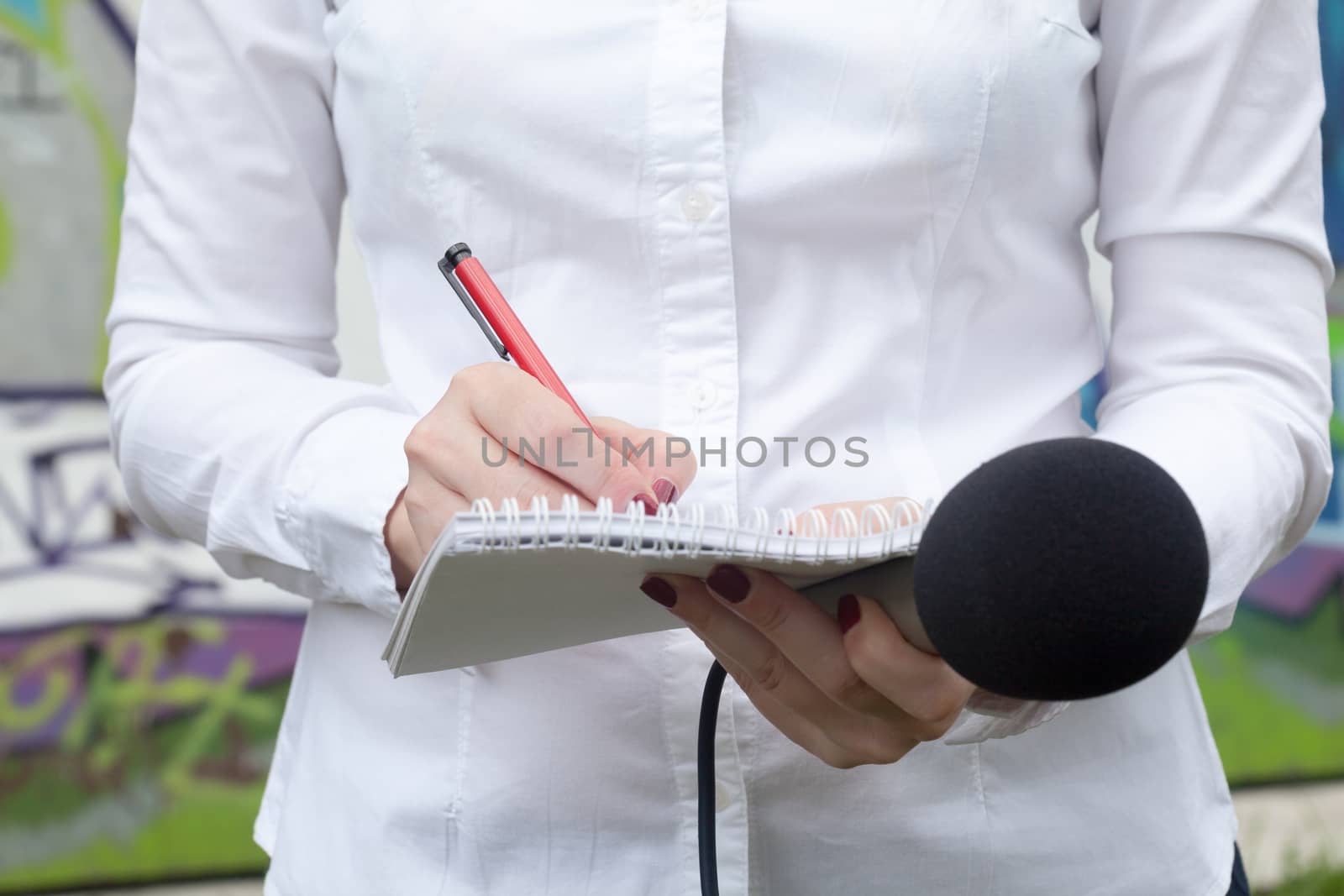 Female reporter or journalist at news conference, writing notes, holding microphone