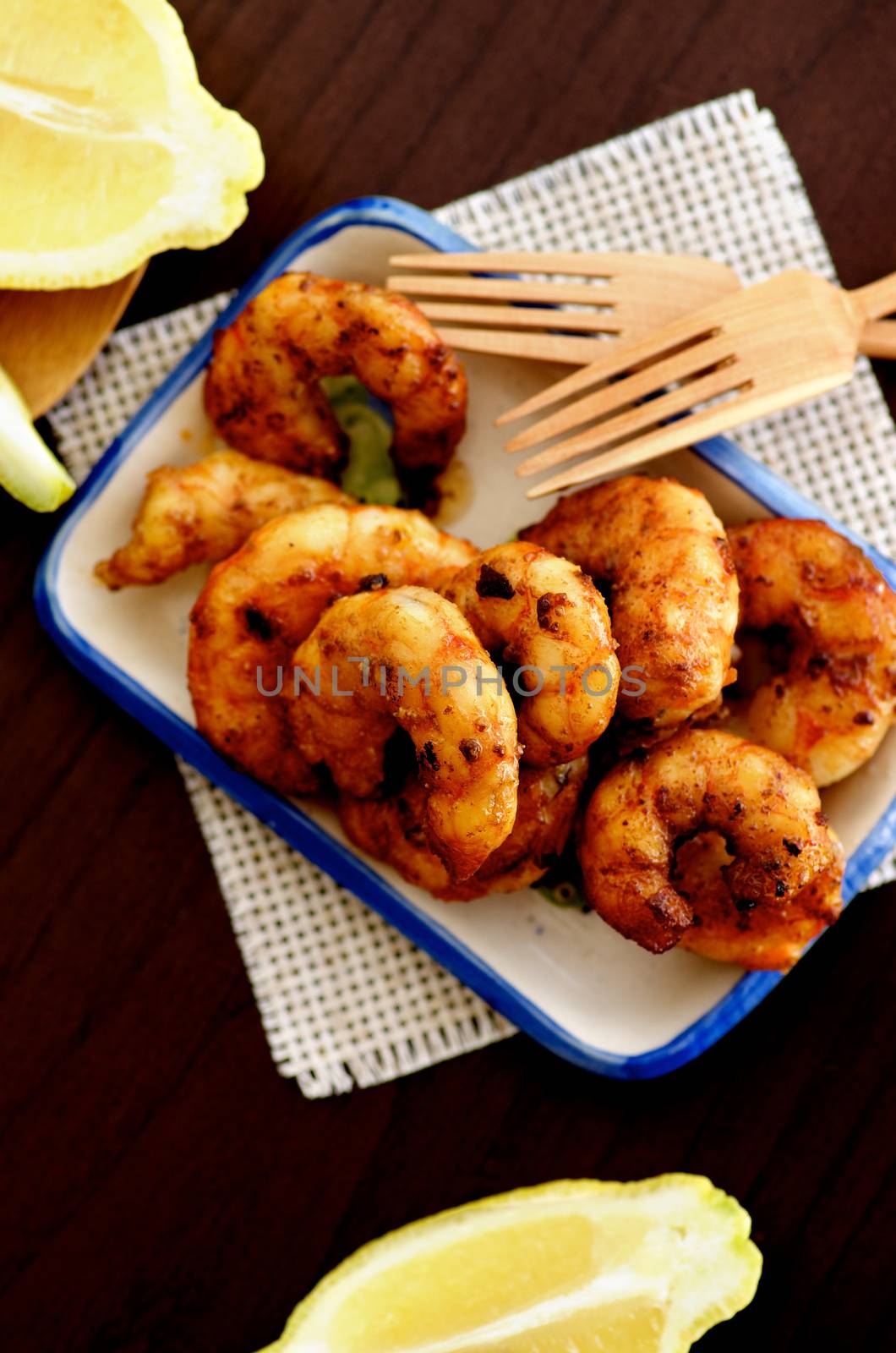 Top View of Delicious Grilled Prawns on Small Plate with Sliced Lemon and Wooden Forks closeup on Wooden Cutting Board. Selective Focus
