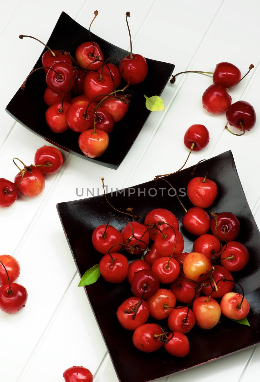 Arrangement of Fresh Ripe Sweet Maraschino Cherries in Black Wooden Plates closeup on Plank White background. Top View