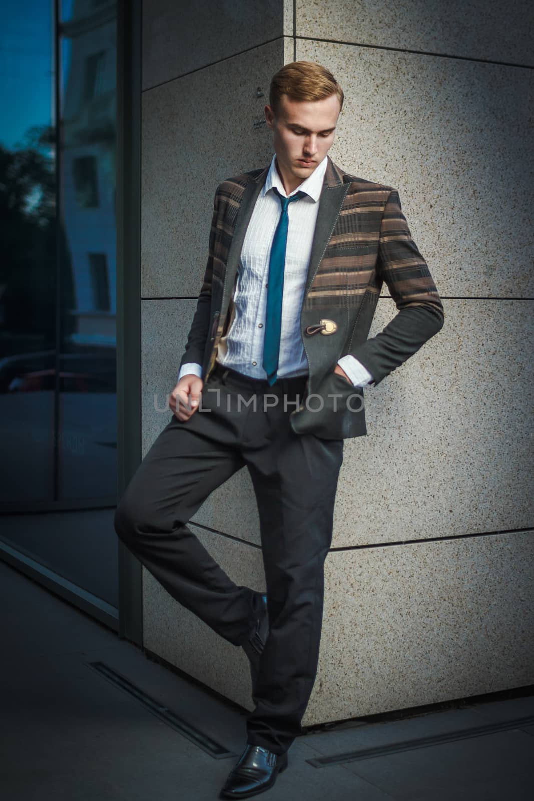 Young handsome successful stylish businessman standing near modern office by mrakor