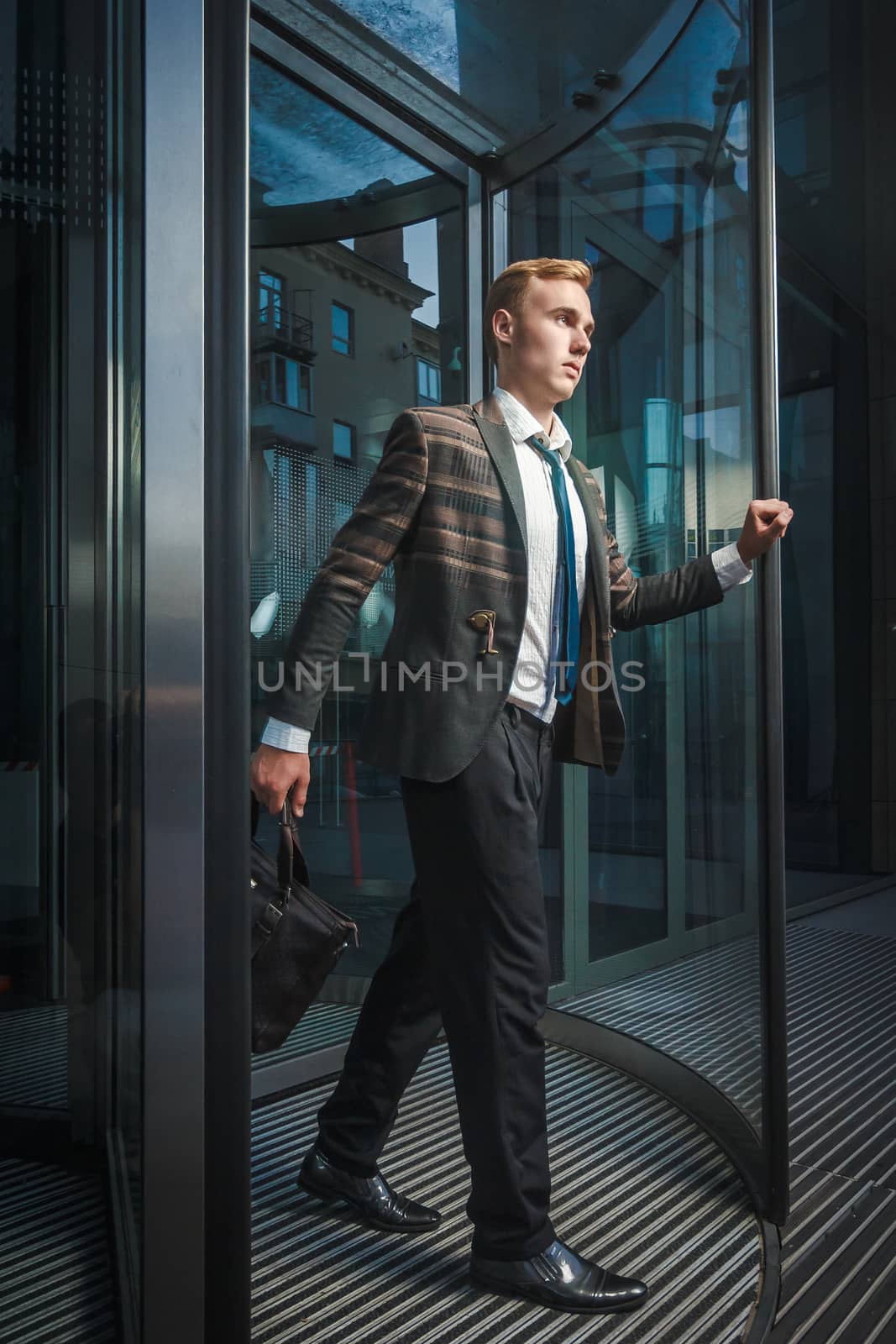 Young handsome successful stylish businessman walking near modern office building. Concept: victory.