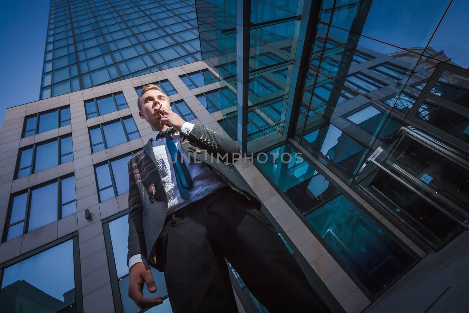 Young handsome successful stylish businessman smoking near modern office by mrakor
