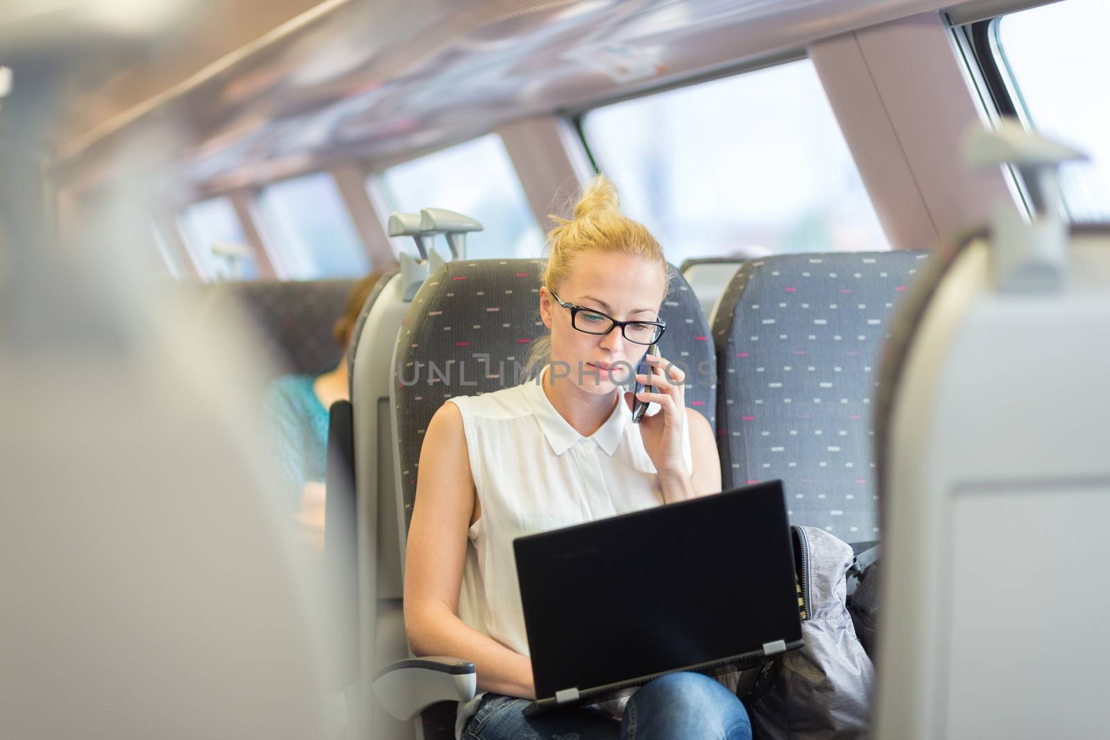 Businesswoman talking on cellphone and working on laptop while traveling by train. Business travel concept.