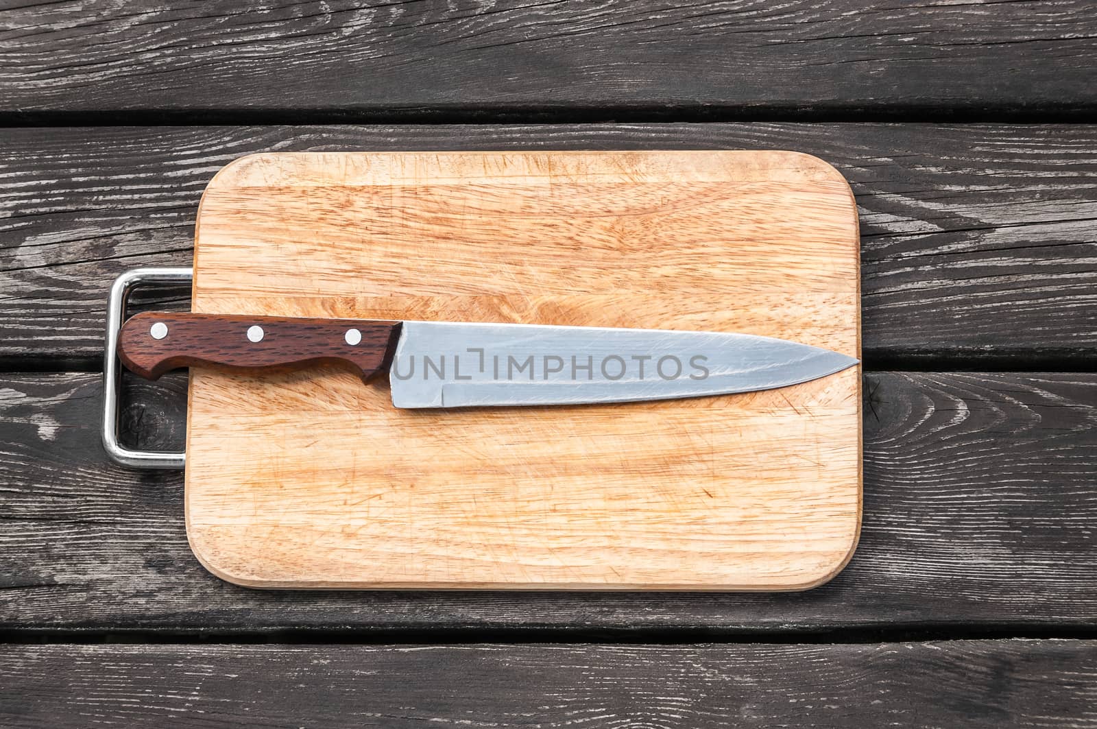 Steel knife on a cutting board on wooden background with