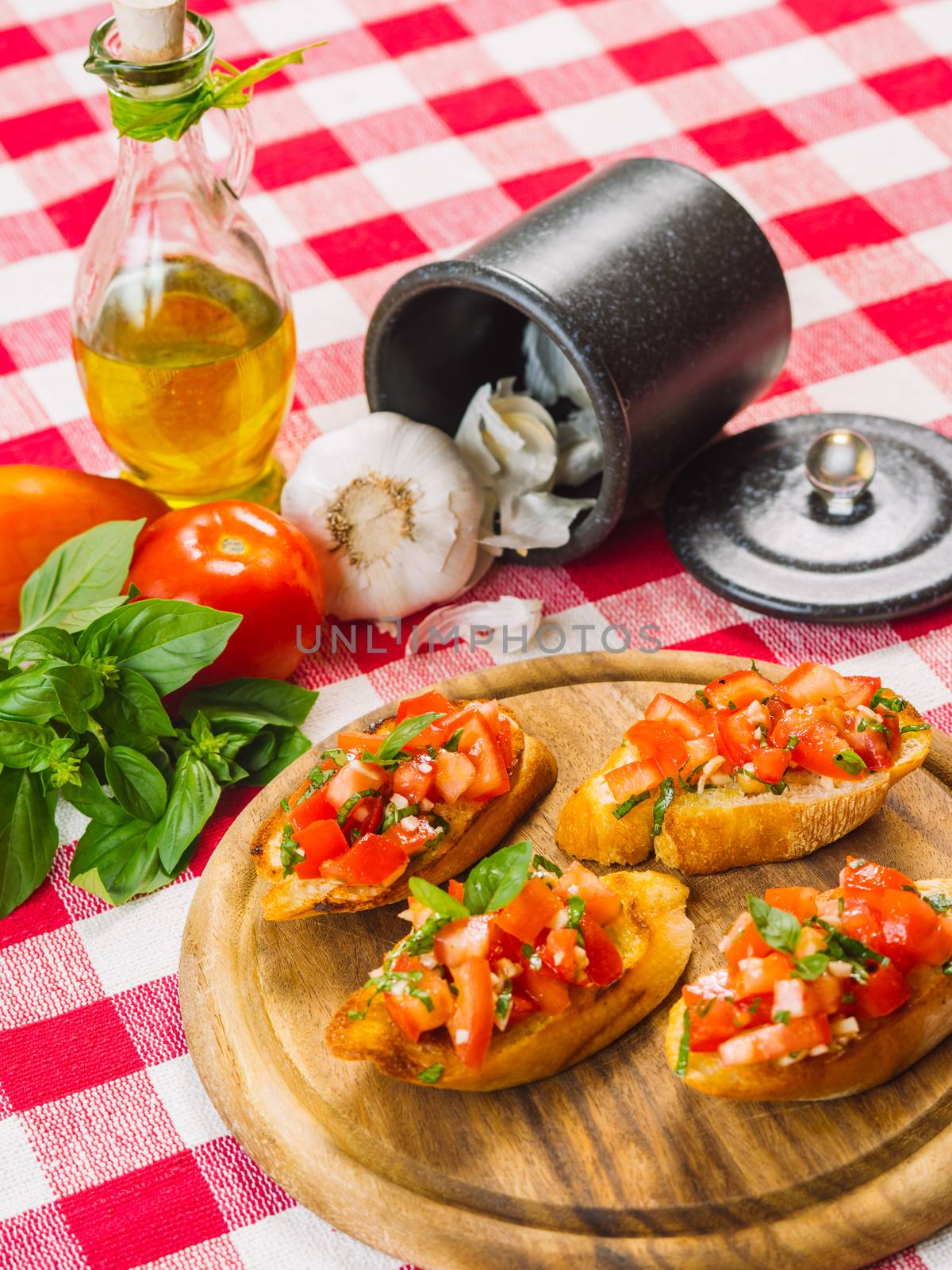 Photo of Italian bruschetta on a wooden board with the ingredients behind. Focus across the middle.
