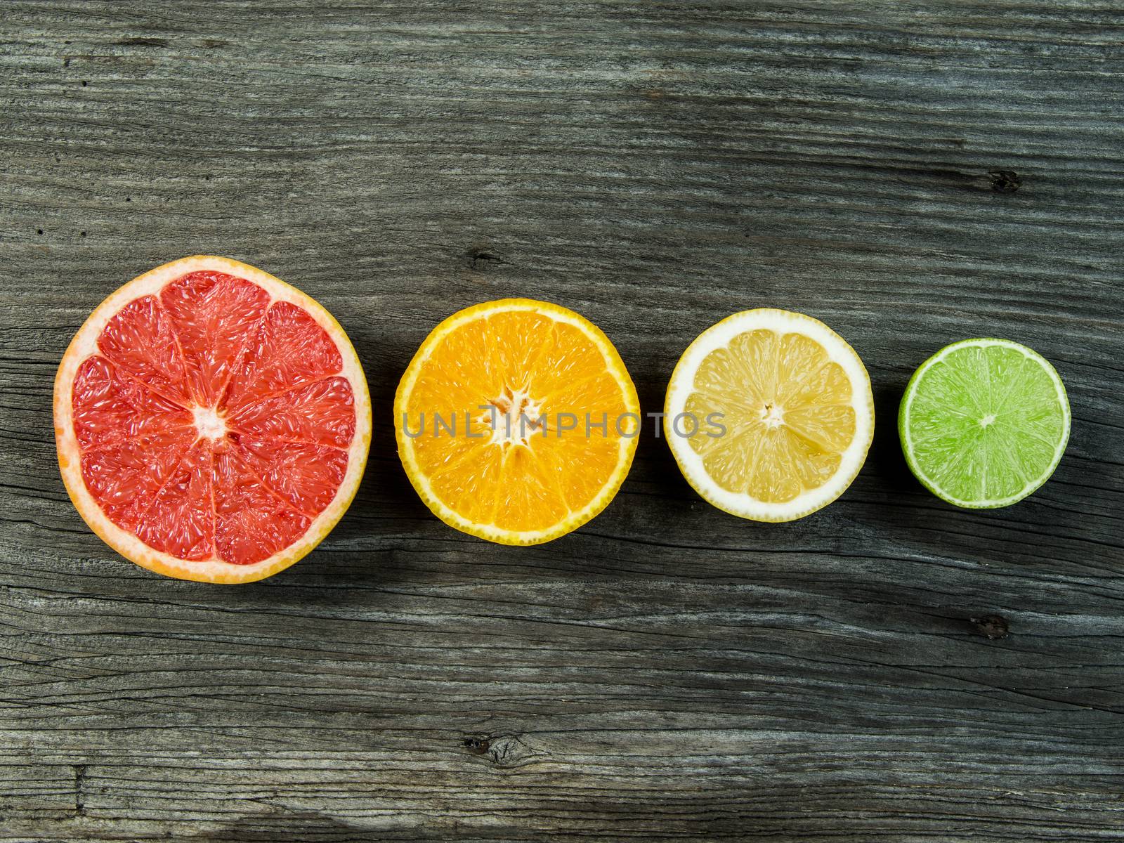 Photo of a sliced grapefruit, orange, lemon, and lime in a row on a old rustic slab of barn board.