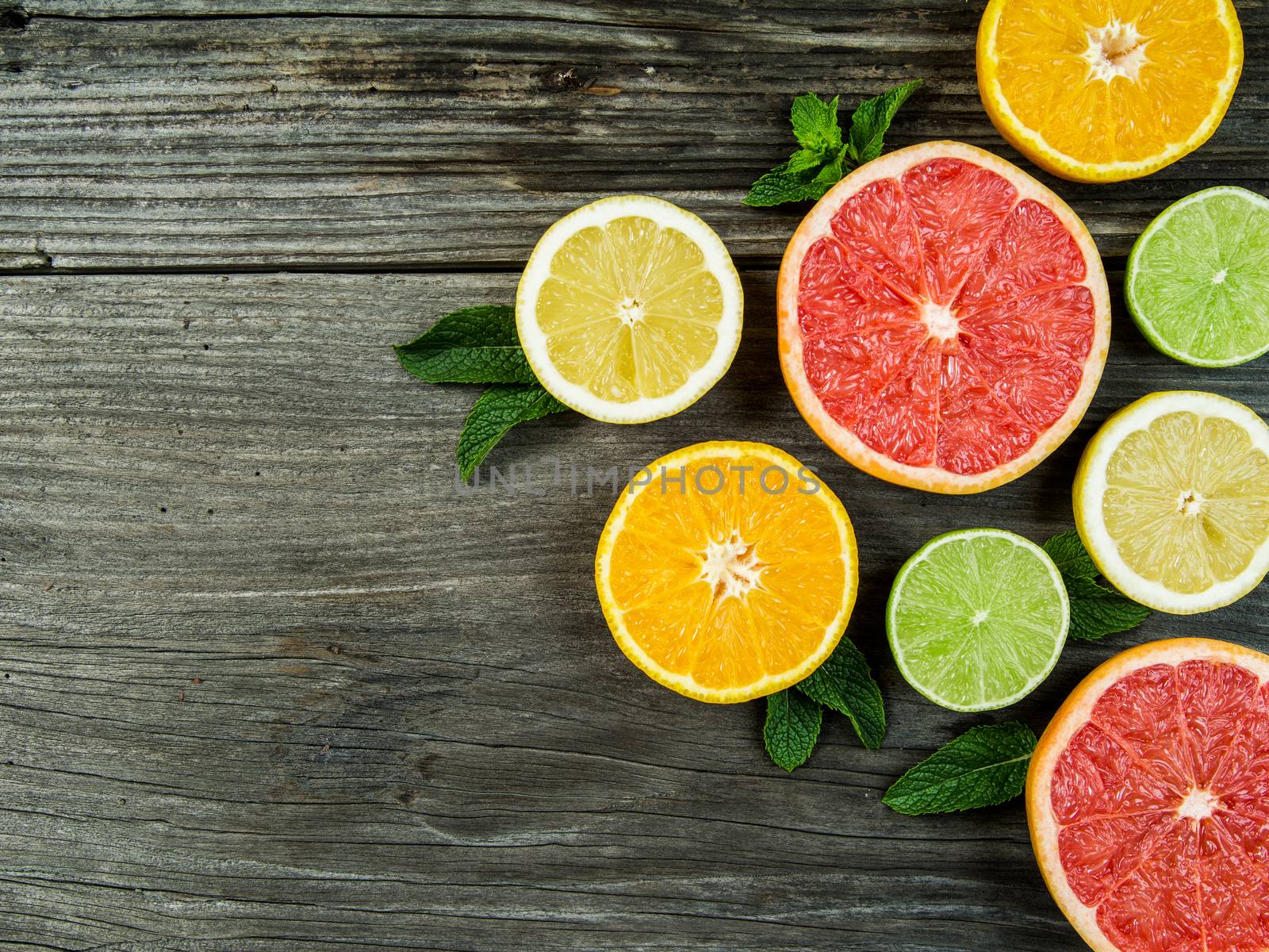 Photo of a sliced grapefruit, orange, lemon, and lime on a old rustic slab of barn board.