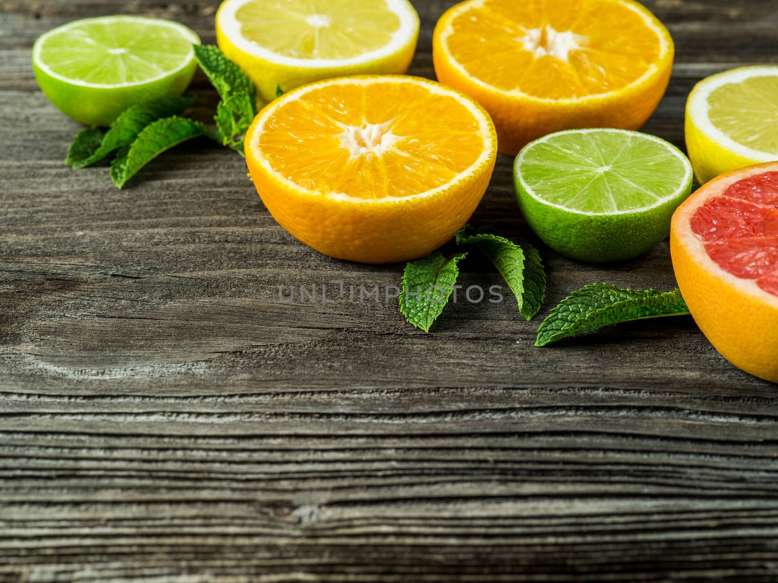 Photo of a sliced grapefruit, orange, lemon, lime, and mint leaves on a old rustic slab of barn board.