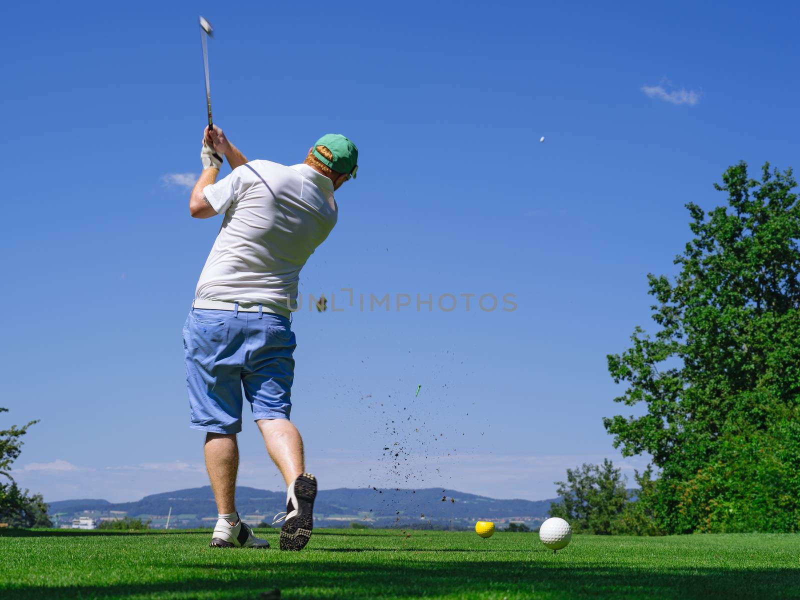 Photo of a male golfer hitting the ball down the fairway on a golf course. Slight motion blur visible.
