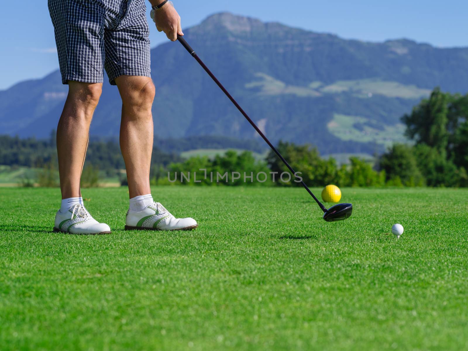 Photo of a male golfer teeing off on a golf course on a beautiful day.