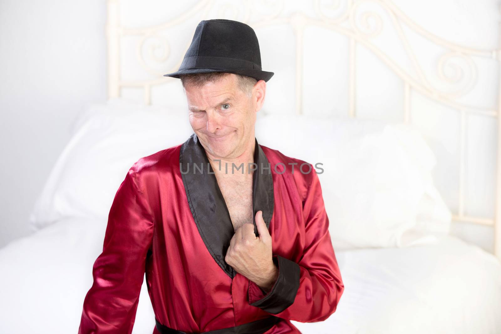 Scheming retro style womanizer in a fedora on white bed
