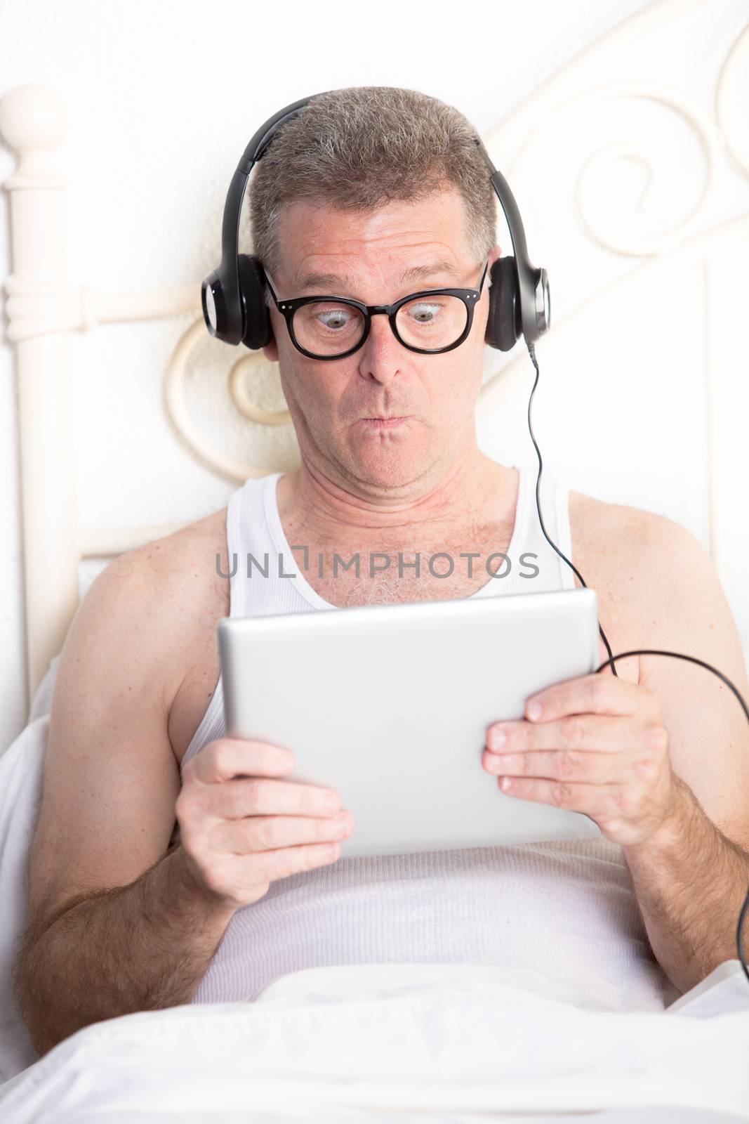 Man in bedroom reacting to content on computer tablet