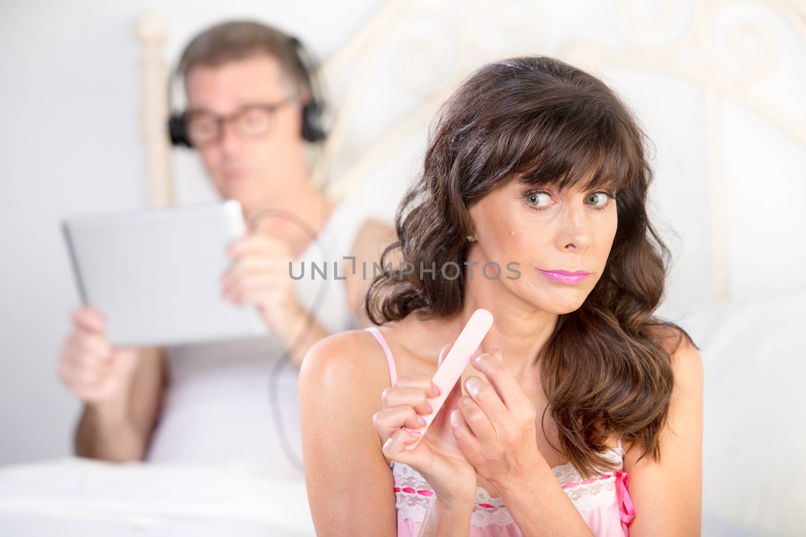 Bored woman and distracted man using tablet computer with headphones in bedroom