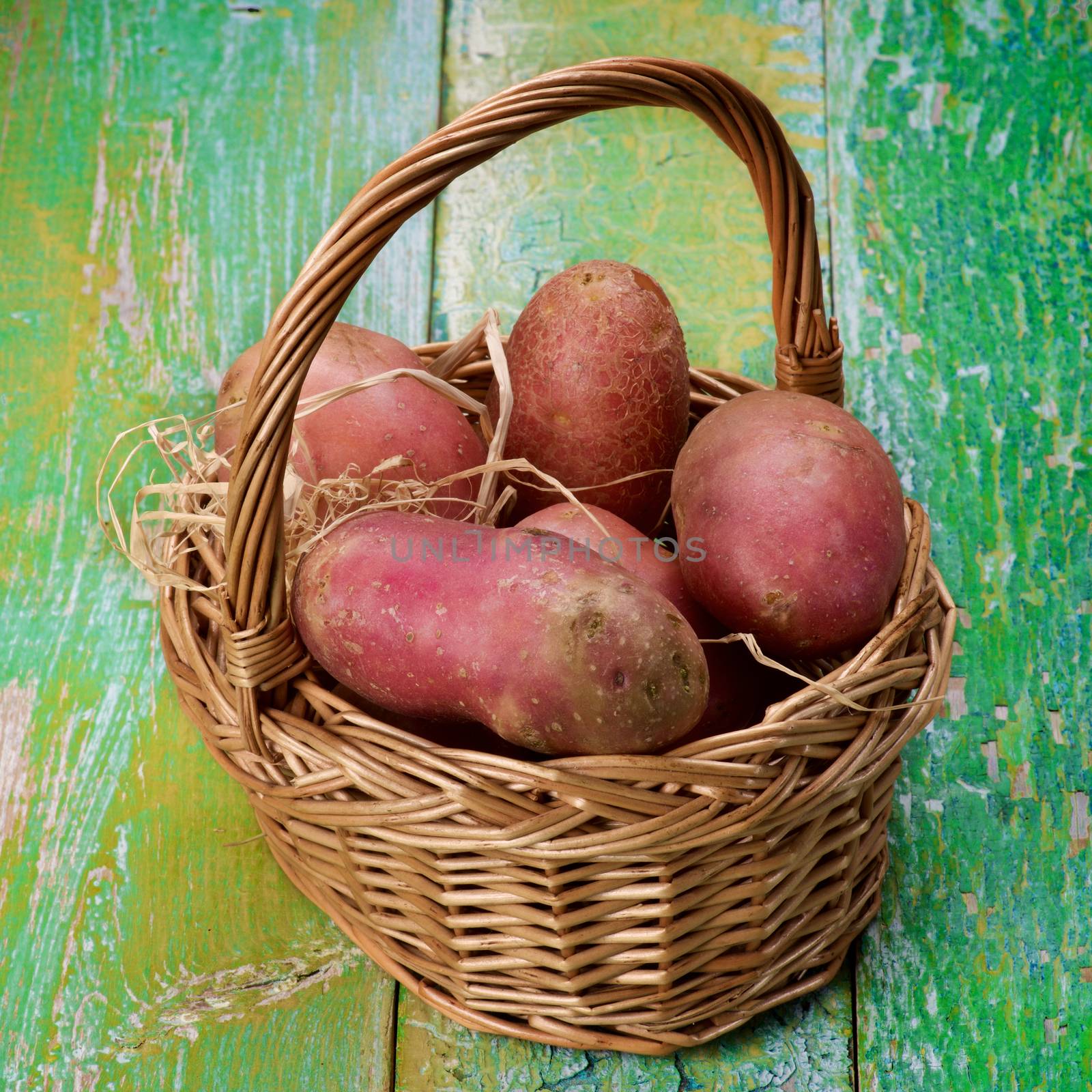 Arrangement of Fresh Raw Red Potatoes in Wicker Basket closeup on Cracked Wooden background
