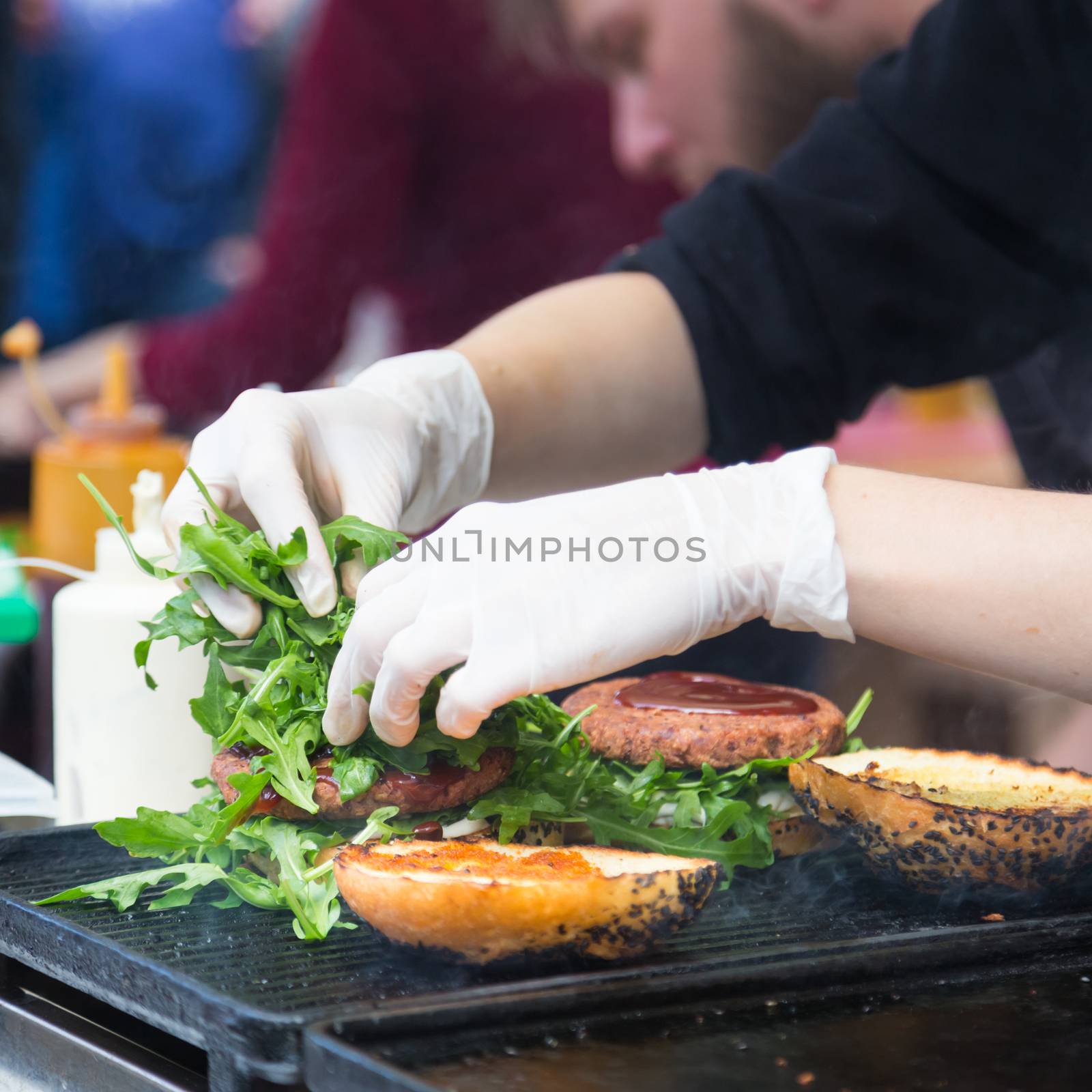 Chef making beef burgers outdoor on open kitchen international food festival event. Street food ready to serve on a food stall.