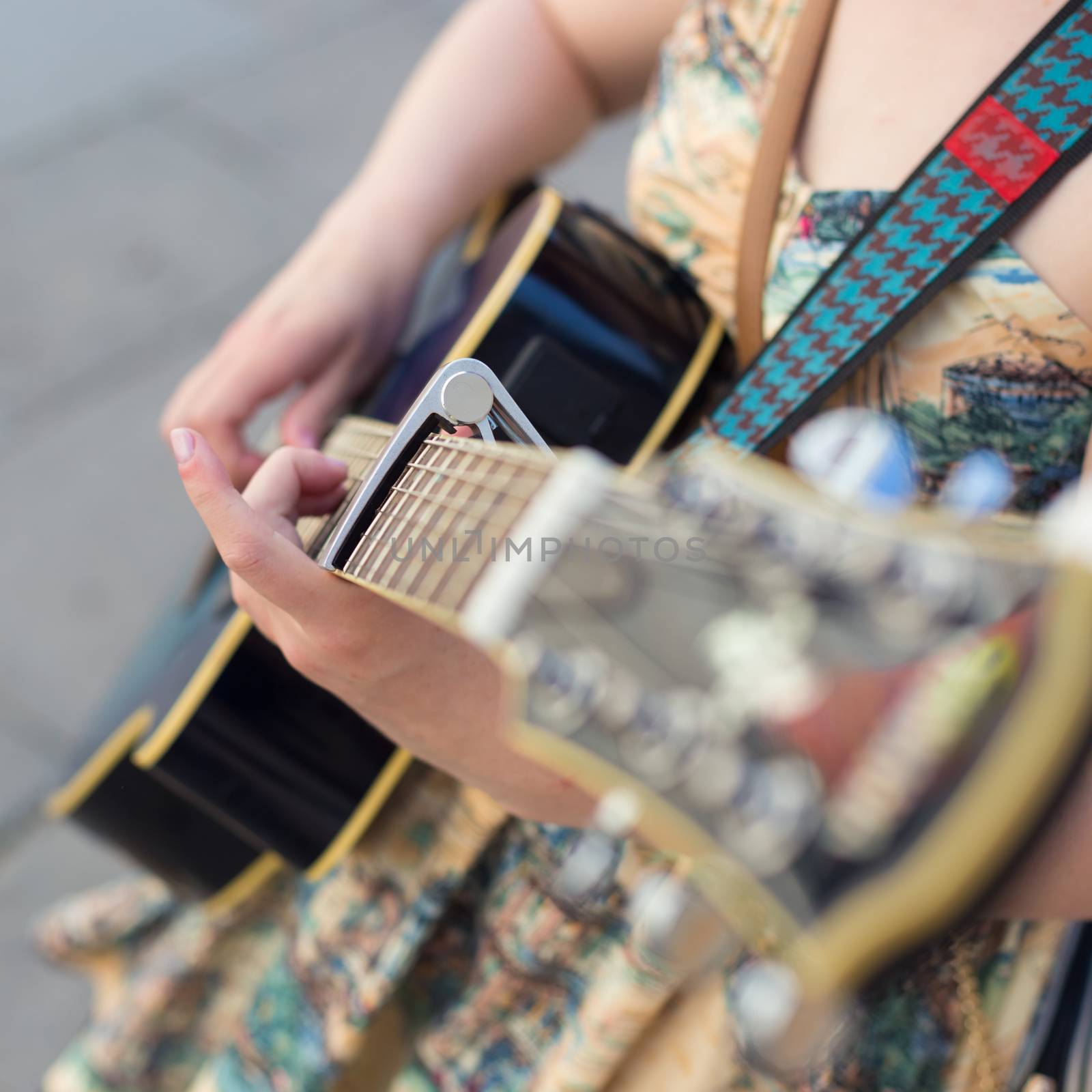 Female street musician playing guitar on sidewalk.