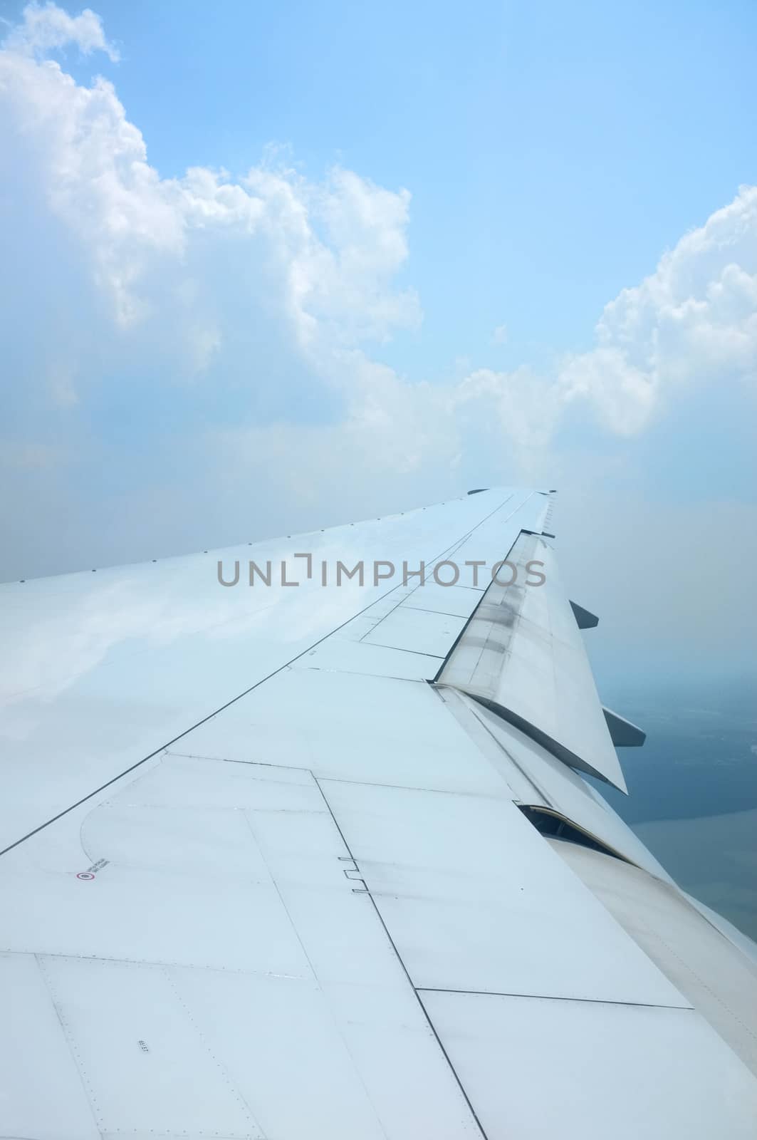 Wing of airplane flying above clouds with nice sky