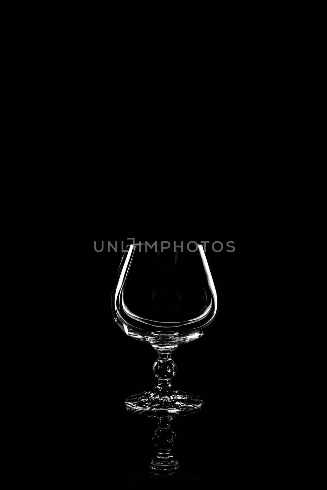 transparent glass for brandy or cognac on black background with reflection