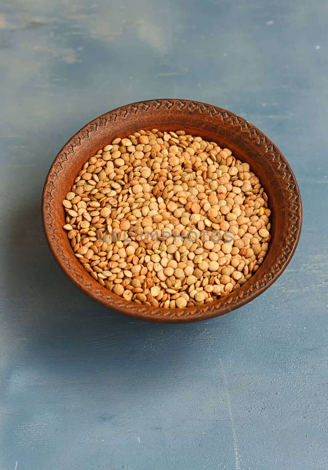 Green lentil in wooden bowl, on blue background