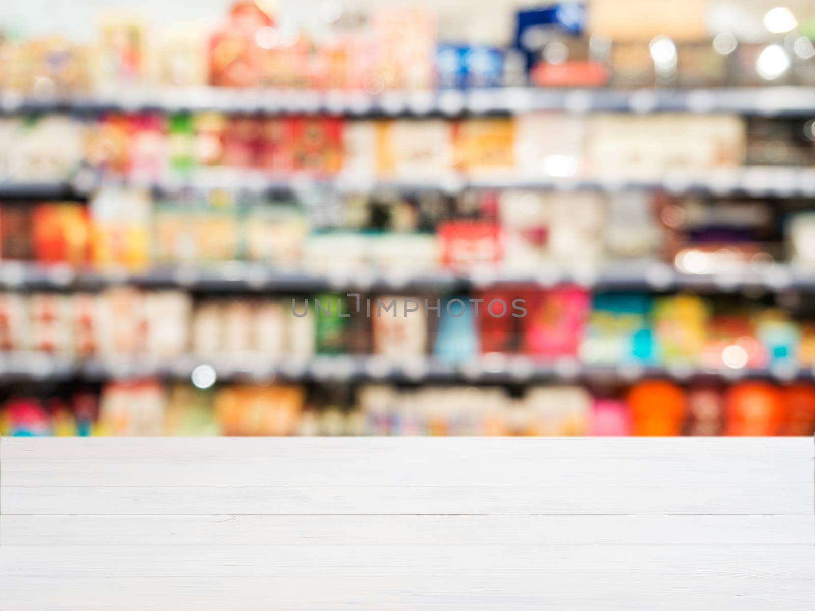 White wooden board empty table in front of blurred background. Perspective white wood board over blurred colorful supermarket products on shelvest - mockup for display of product