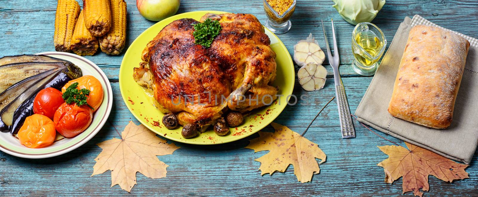Kitchen table with baked chicken in vegetables and strewn with autumn leaves