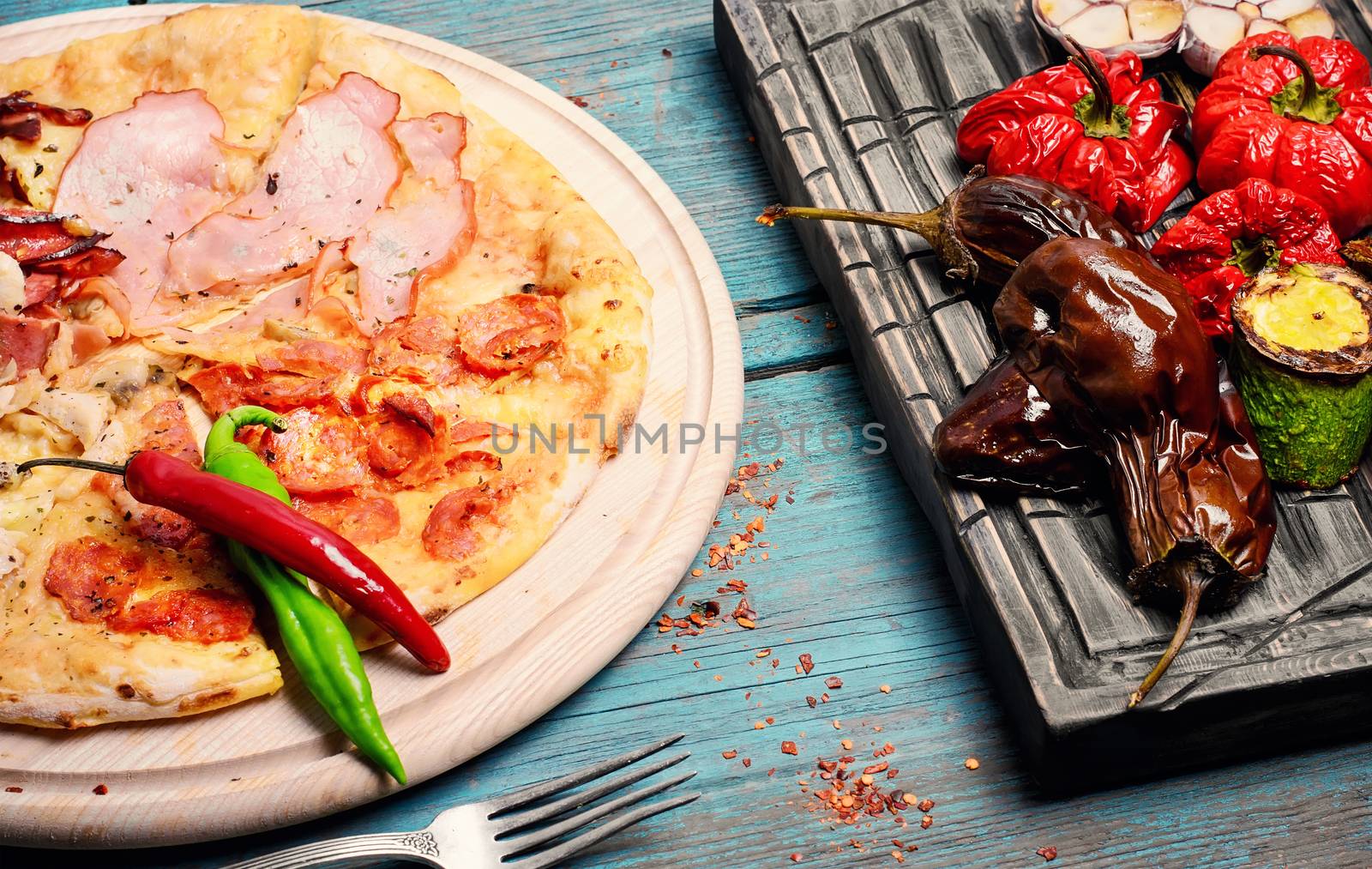 Italian pizza with meat and baked vegetables on the kitchen board