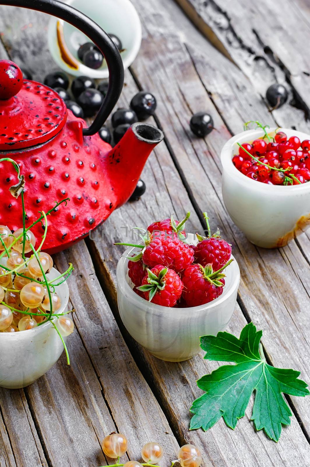 Kettle and summer berries currants and raspberries on wooden background