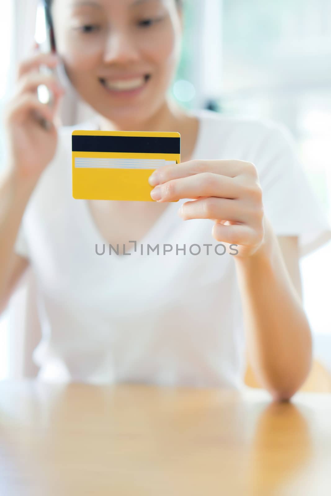 Closeup on credit card in hand of female speaking mobile by ekachailo