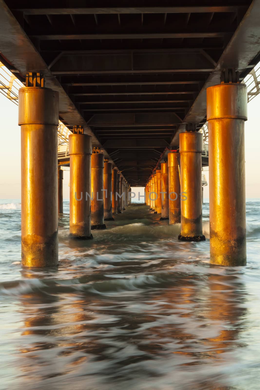View of seascape from under a piermarine pillars lit by morning sun