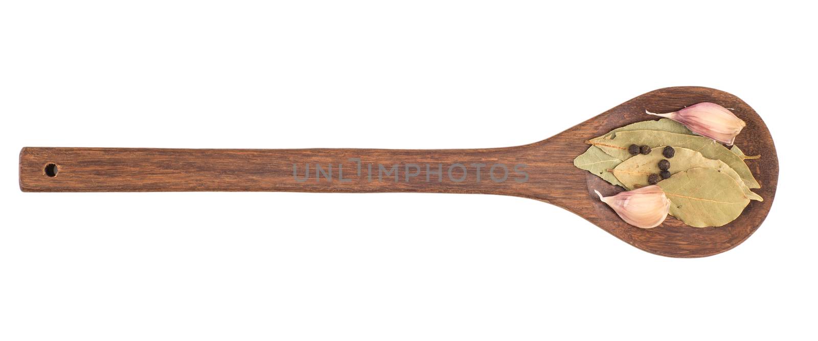 Garlic in a wooden spoon with bay leaf herb and black peppercorns isolated over white background.