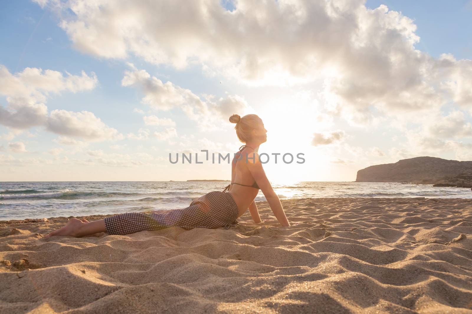 Active young woman streching and practicing yoga on beach at sunset.