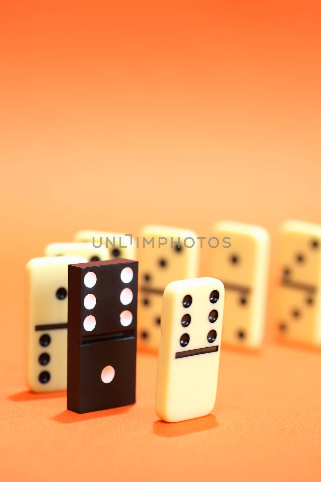 Black domino among white dominoes standing in a row on red background