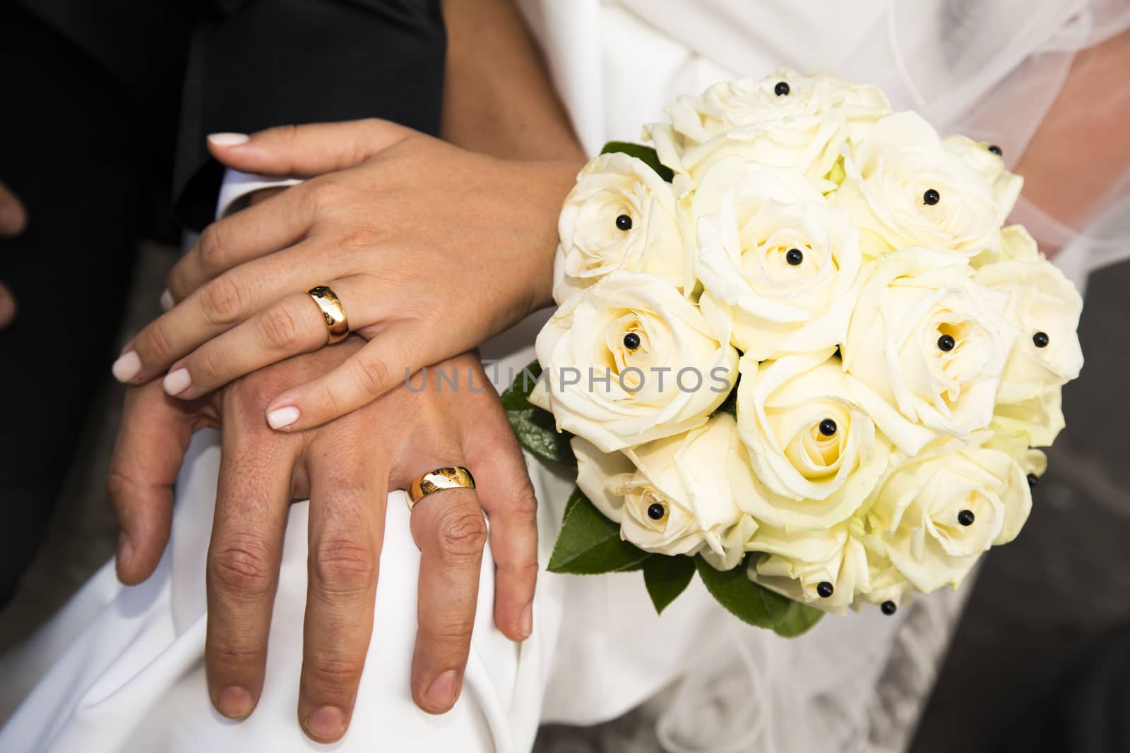 Close-up view of a bridal bouquet made of roses pale yellow and hands of the couple in the background