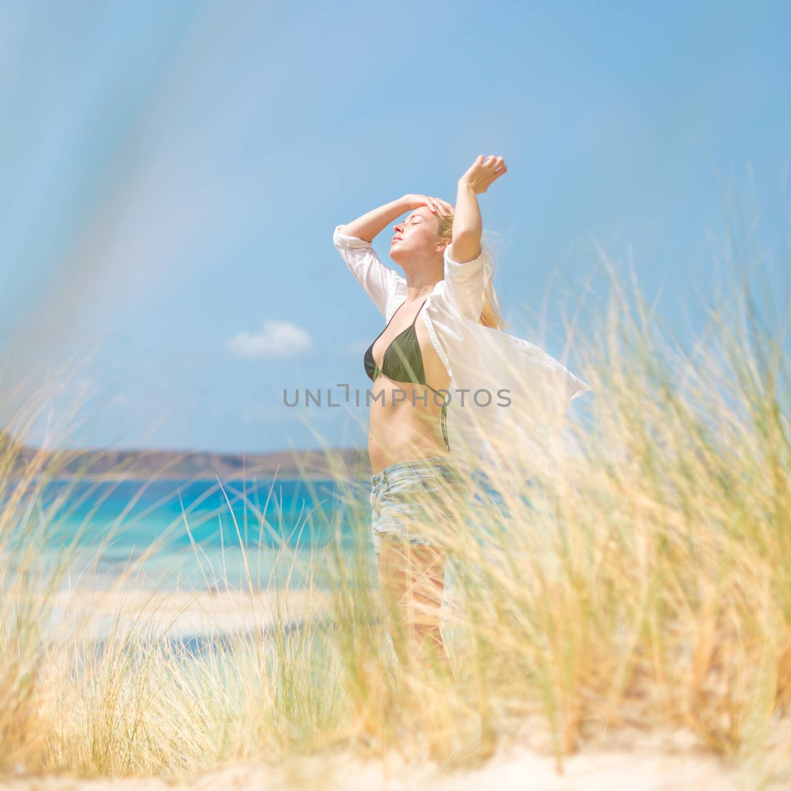 Relaxed woman enjoying sun, freedom and life an a beautiful beach. Young lady feeling free, relaxed and happy. Concept of vacations, freedom, happiness, enjoyment and well being.