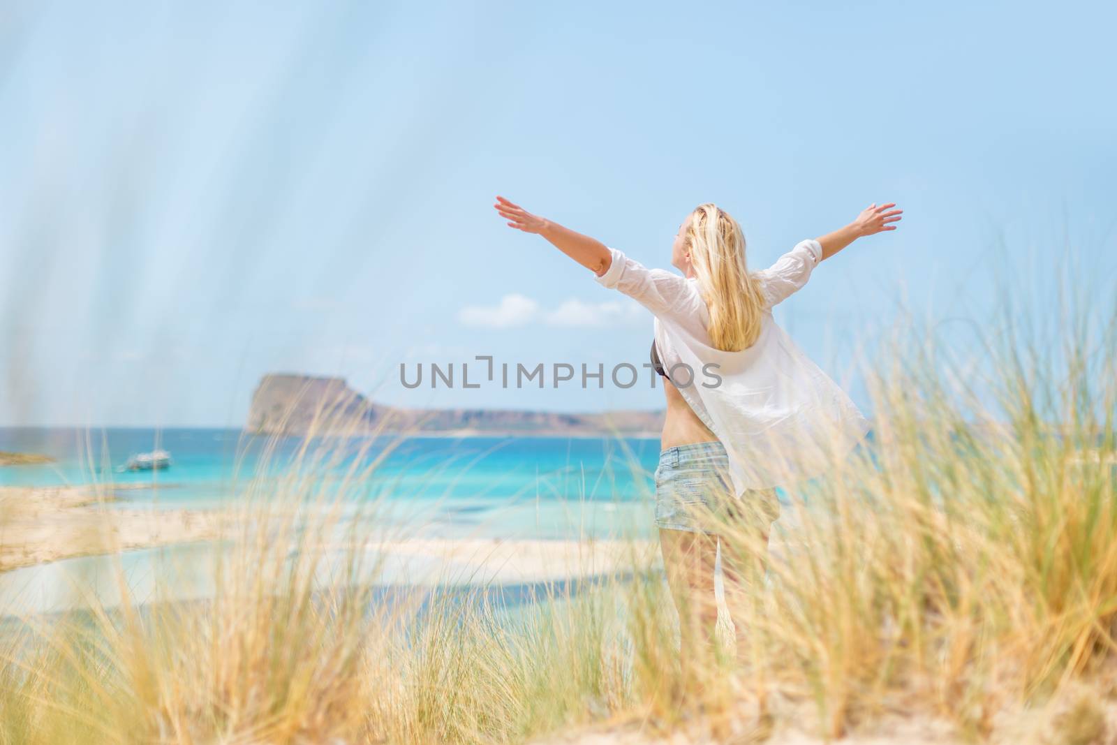 Relaxed woman, arms rised, enjoying sun, freedom and life an a beautiful beach. Young lady feeling free, relaxed and happy. Concept of vacations, freedom, happiness, enjoyment and well being.