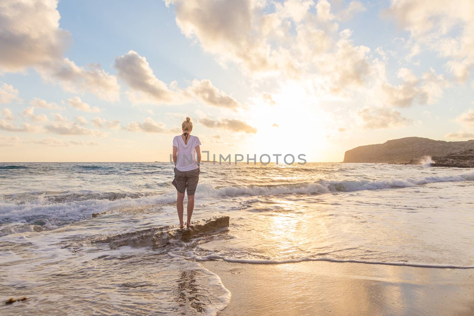 Relaxed woman enjoying sun, freedom and life an beautiful beach in sunset. Young lady feeling free, relaxed and happy. Concept of vacations, freedom, happiness, enjoyment and well being.