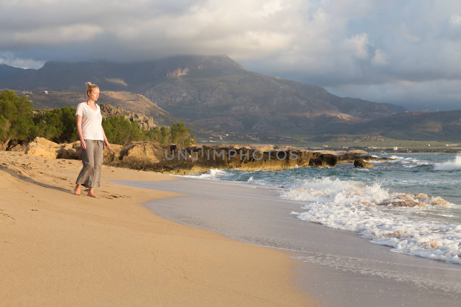 Woman walking on sand beach at golden hour. Seashore sunset walk.