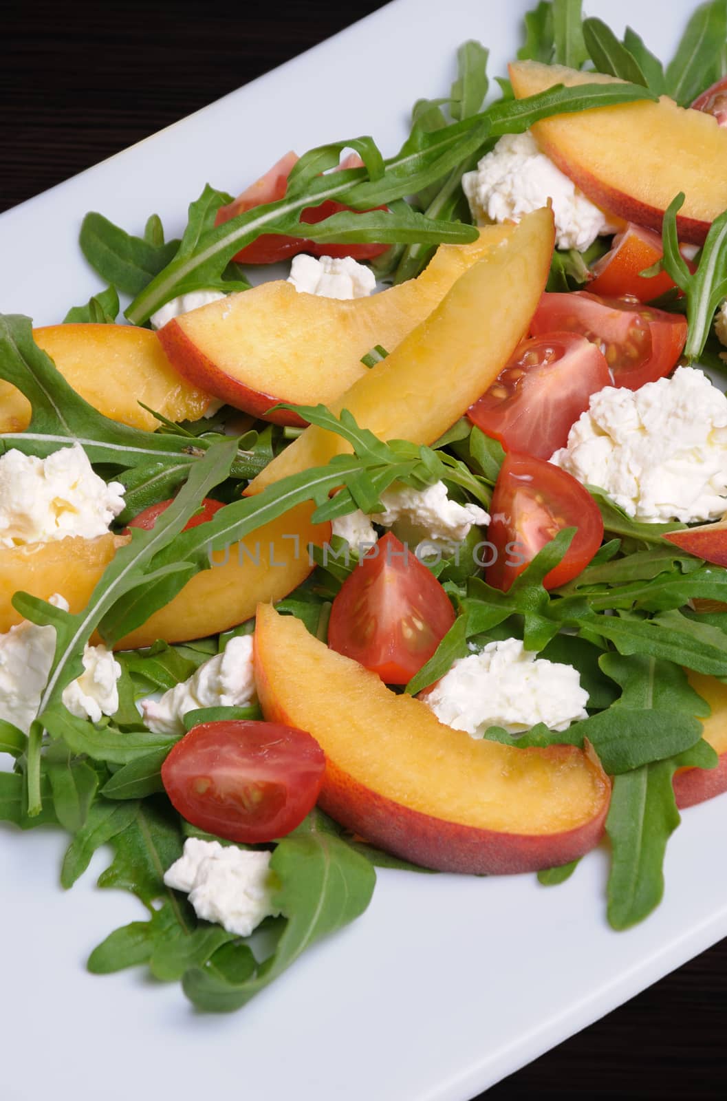 Salad with slices of peach, cherry tomatoes, arugula, feta