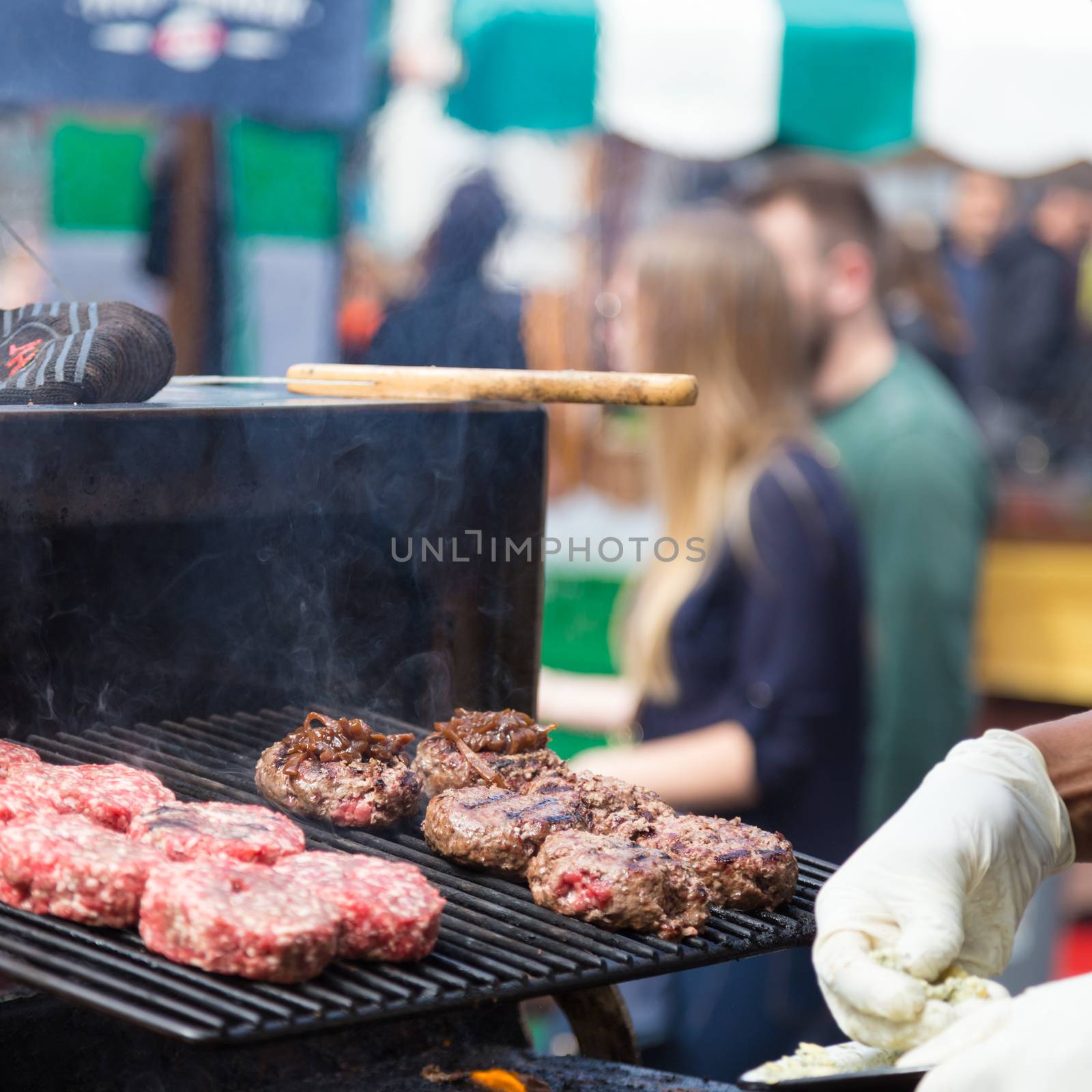 Chef making beef burgers outdoor on open kitchen international food festival event. Street food ready to serve on a food stall.