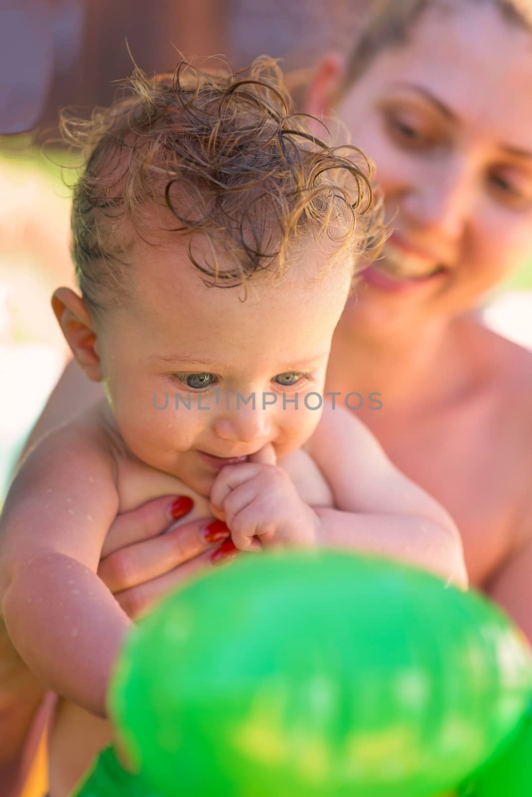 Baby boy, looks surprised a toy helped by mum smiling in background