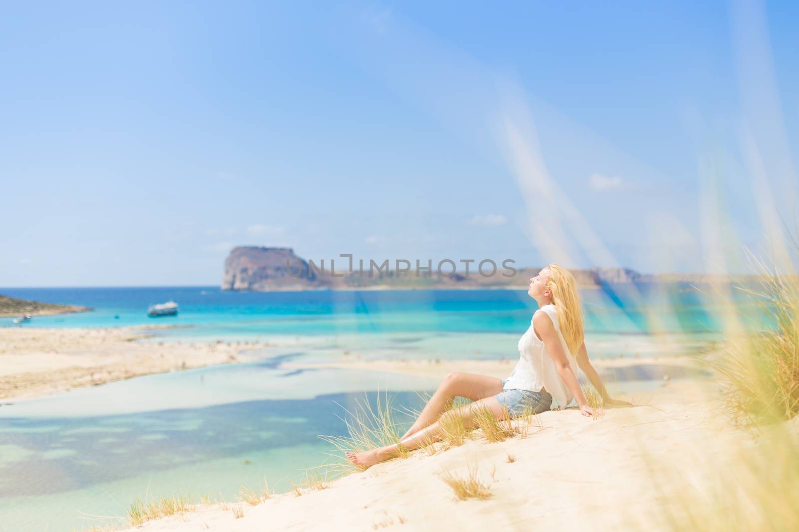 Relaxed woman enjoying sun, freedom and life an a beautiful sandy beach of Balos in Greece. Young lady feeling free, relaxed and happy. Vacations, freedom, happiness, enjoyment and well being.