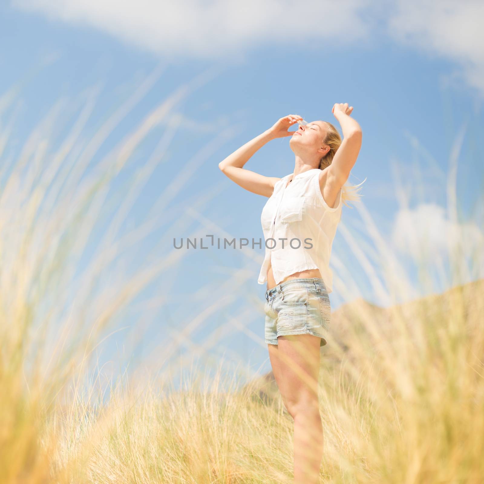 Relaxed woman, arms rised, enjoying sun, freedom and life an a beautiful beach. Young lady feeling free, relaxed and happy. Concept of vacations, freedom, happiness, enjoyment and well being.