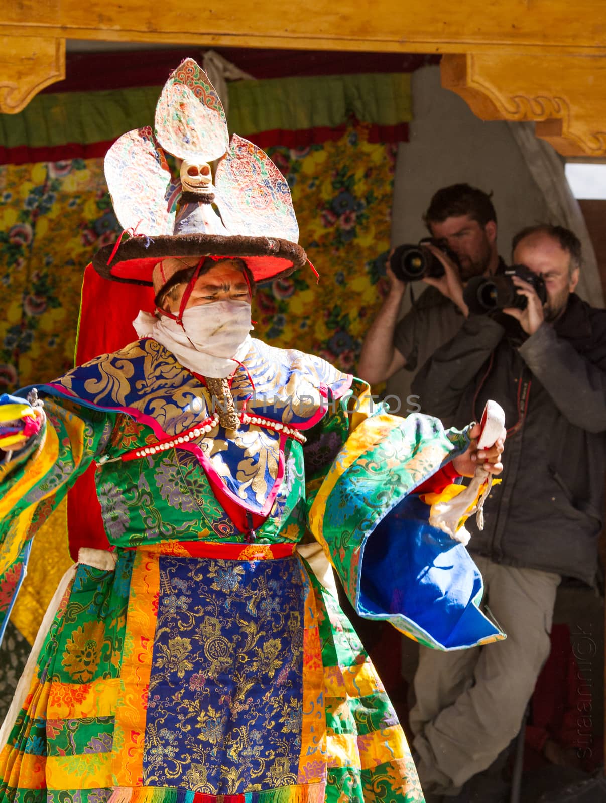 Kursha, India - July 17, 2012: Lama performs a religious masked and costumed mystery black hat dance of Tibetan Buddhism during the Cham Dance Festival, with two photographers on the background in Kursha monastery, India.