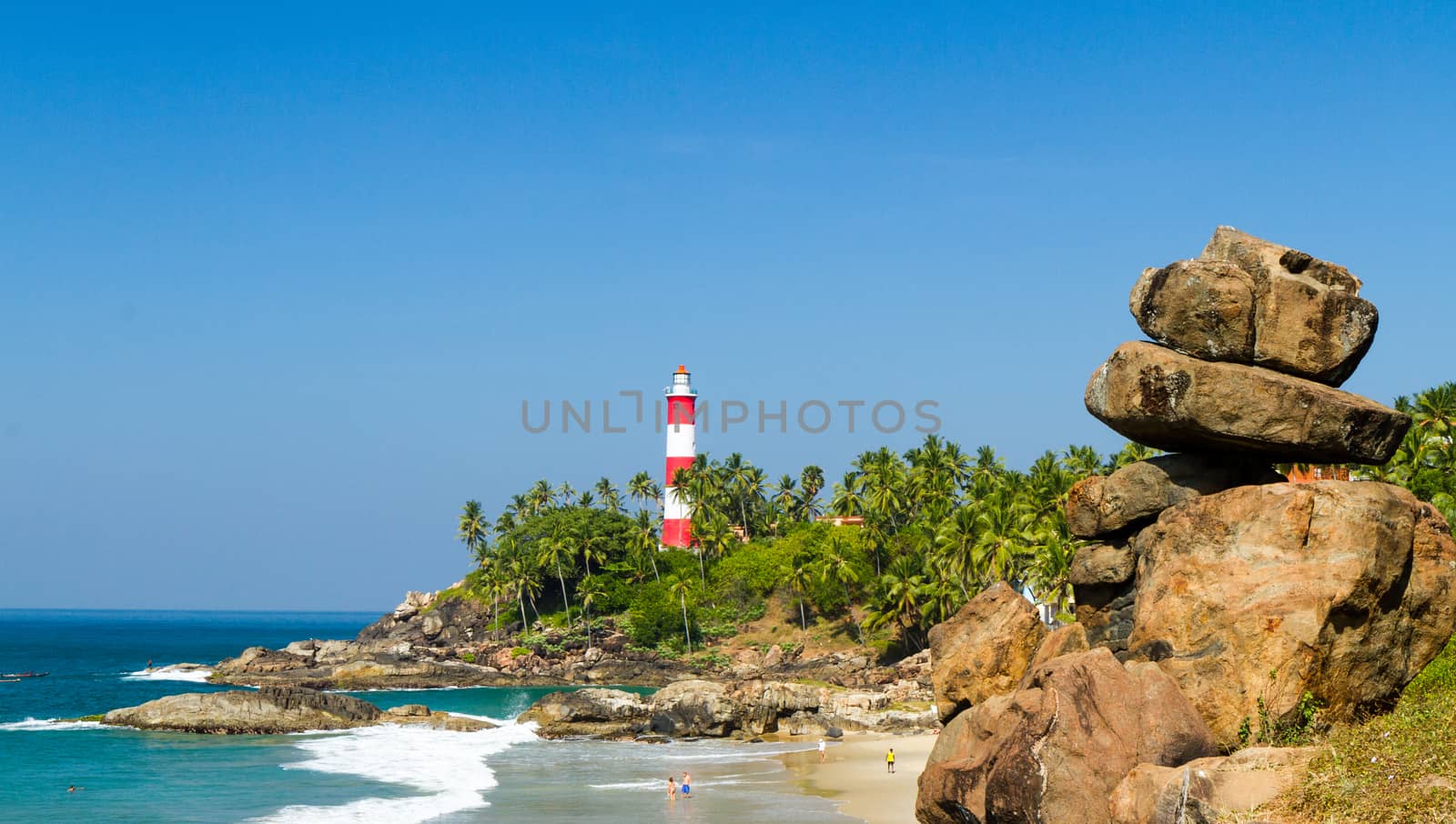 Маяк на мысе, уходящем в Аравийское море и пляж со скалами на переднем плане на курорте в Керале в солнечную погоду (southern India) by straannick