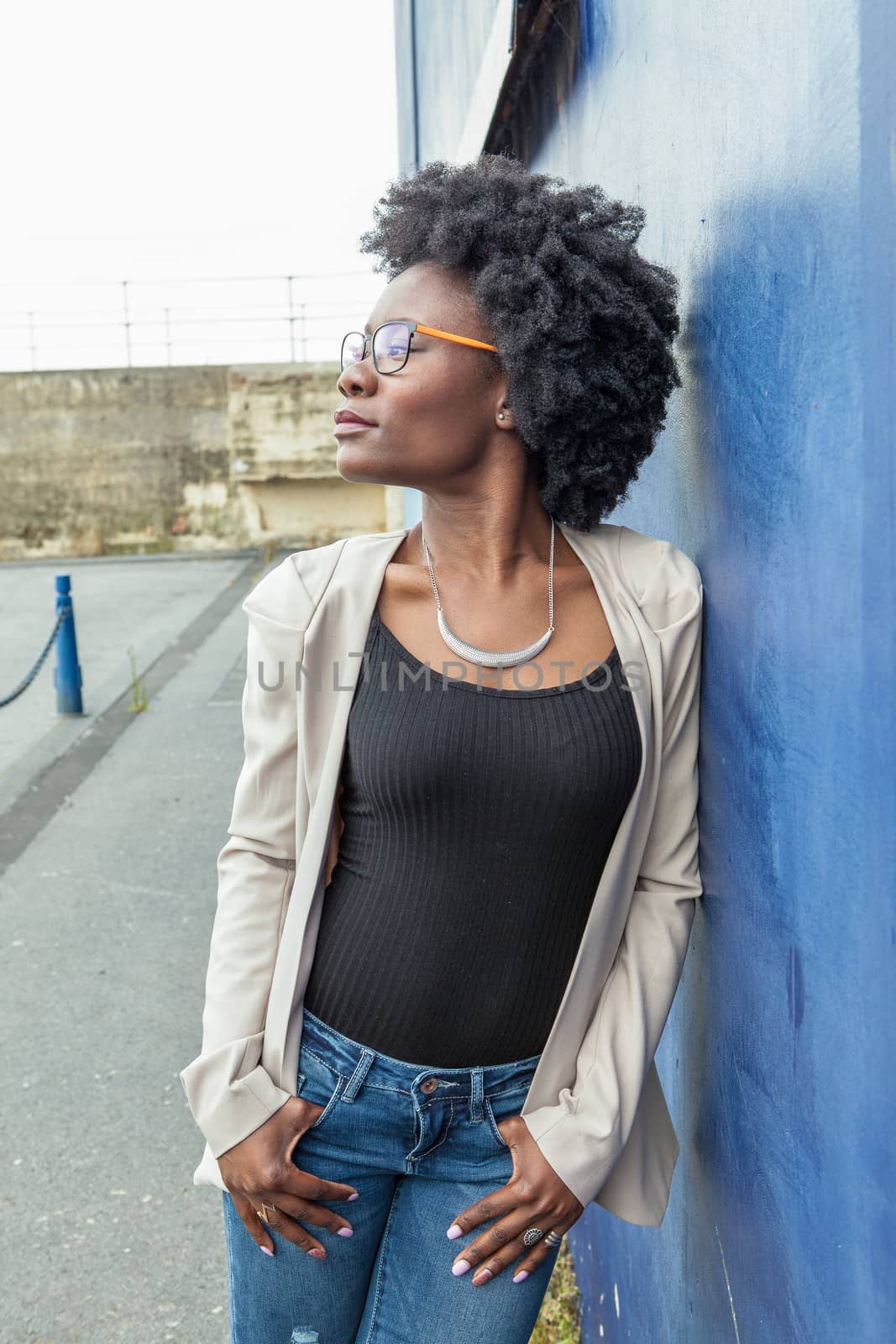 Young African woman standing on a blue wall in the background