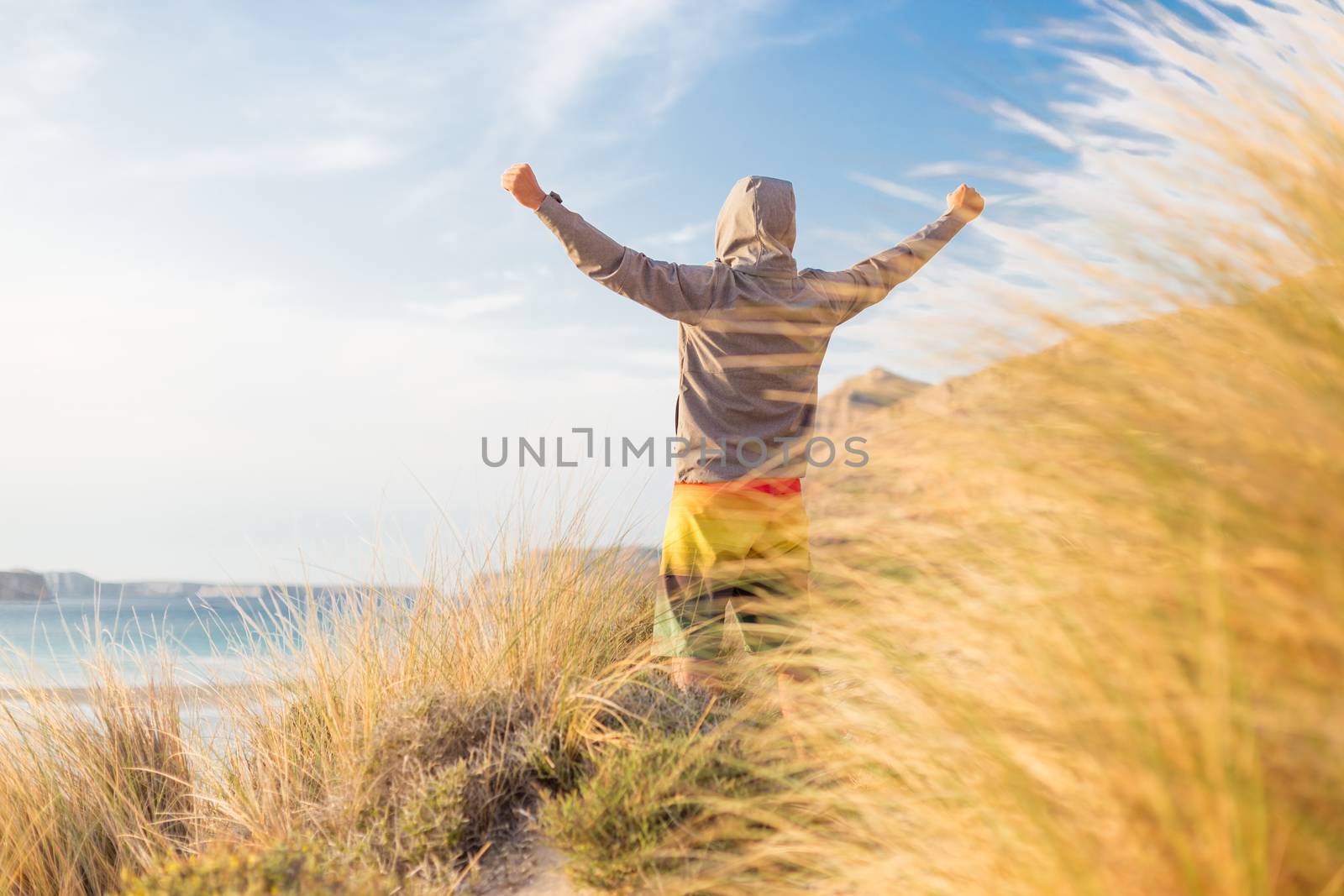 Successful sporty active man, arms rised, enjoying beauty of nature, freedom and life at beautiful landscape at Balos beach, Greece. Active lifestyle outdoors. Made it.