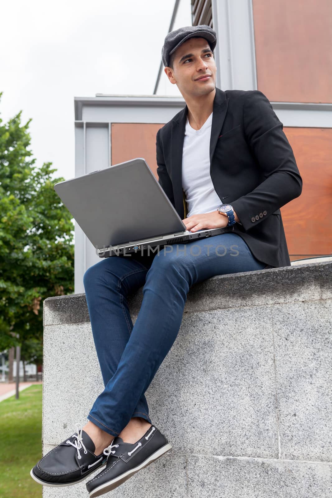 Young man with Irish beret sitting on a wall with his laptop
